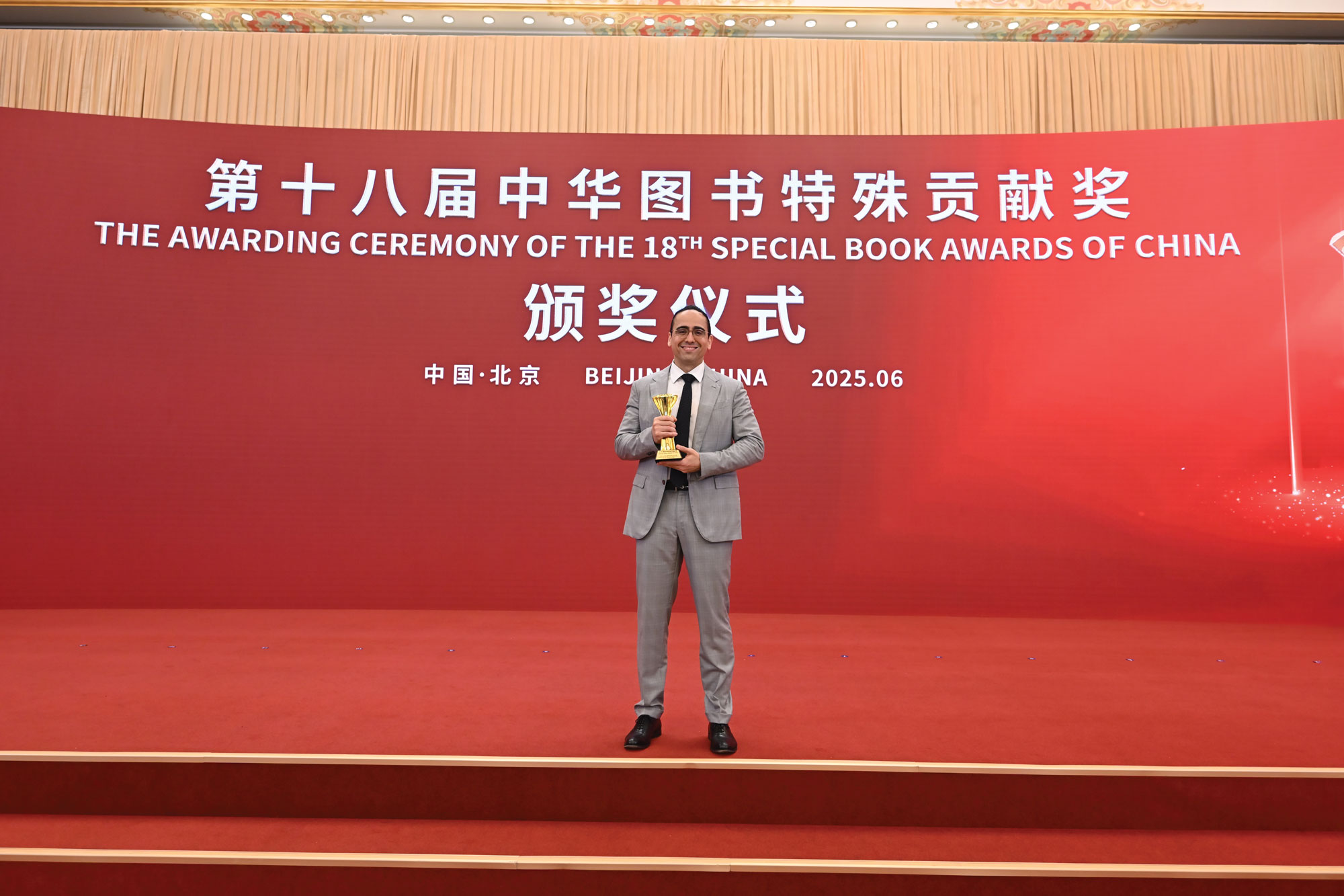 Sinedino stands on stage in Beijing with his prize from the State Press and Publication Administration